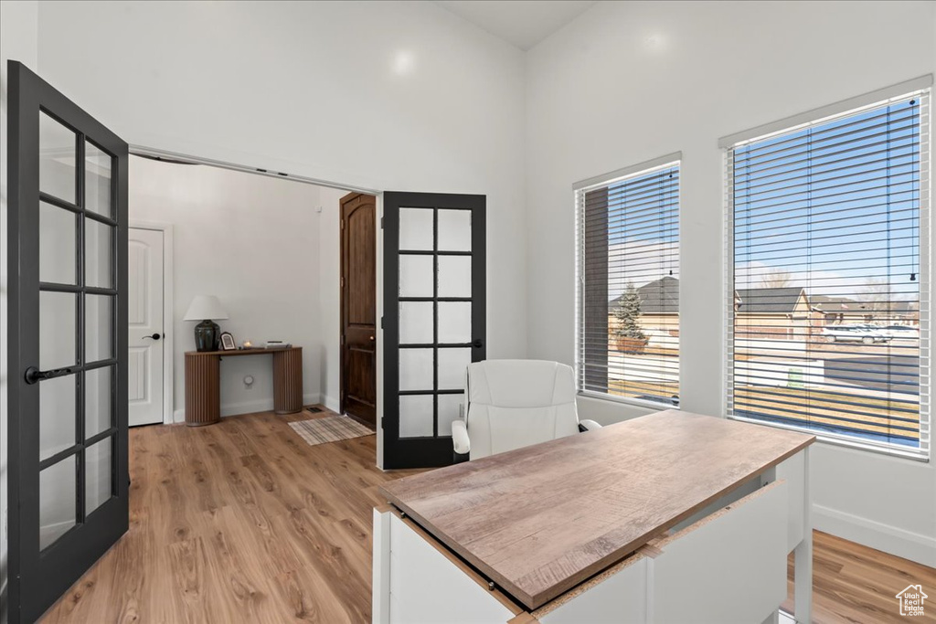 Home office with french doors, a high ceiling, and light hardwood / wood-style flooring