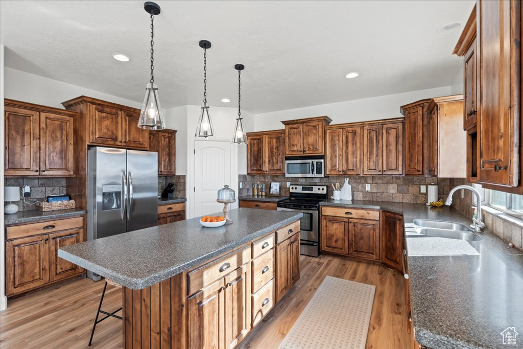 Kitchen with a kitchen island, appliances with stainless steel finishes, decorative light fixtures, sink, and light hardwood / wood-style flooring