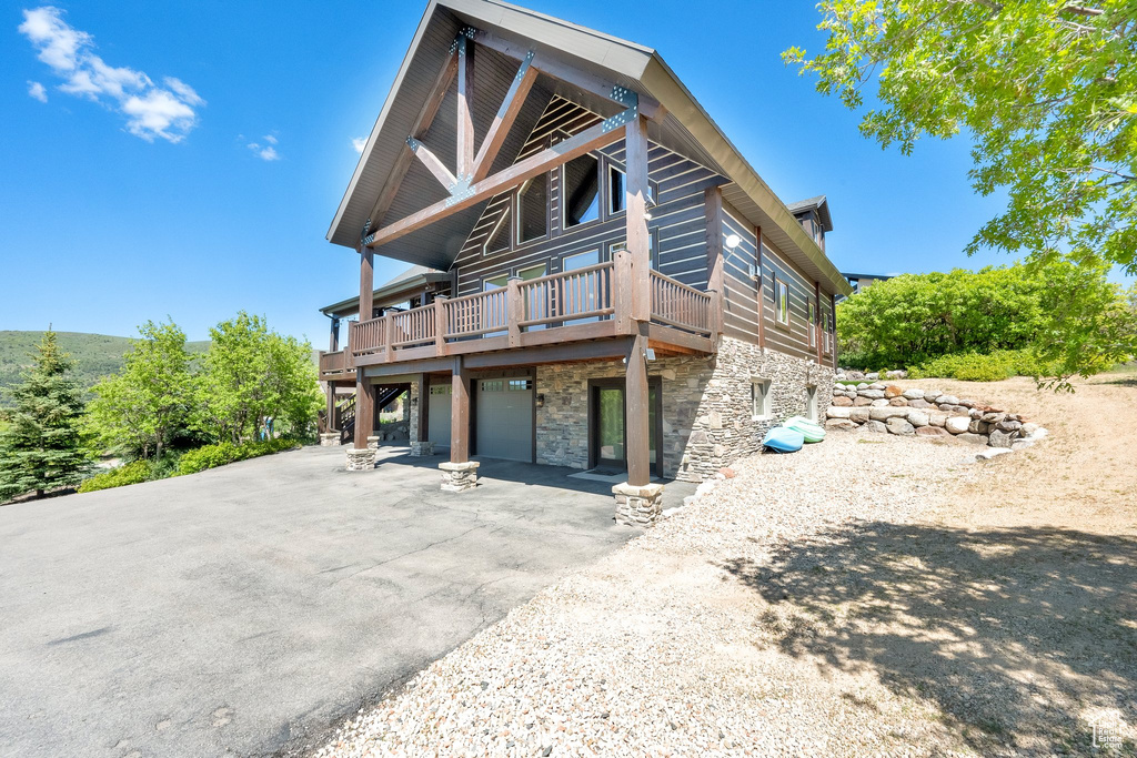 View of front of property with stone siding, asphalt driveway, a garage, and a deck