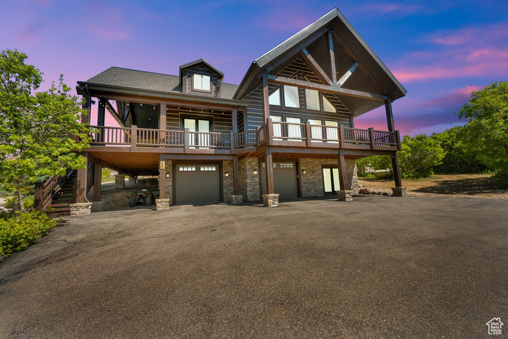 View of front of property featuring stone siding, driveway, an attached garage, a wooden deck, and stairs