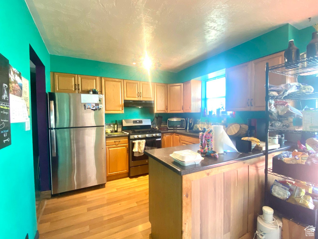 Kitchen with appliances with stainless steel finishes, light brown cabinetry, kitchen peninsula, and light hardwood / wood-style flooring