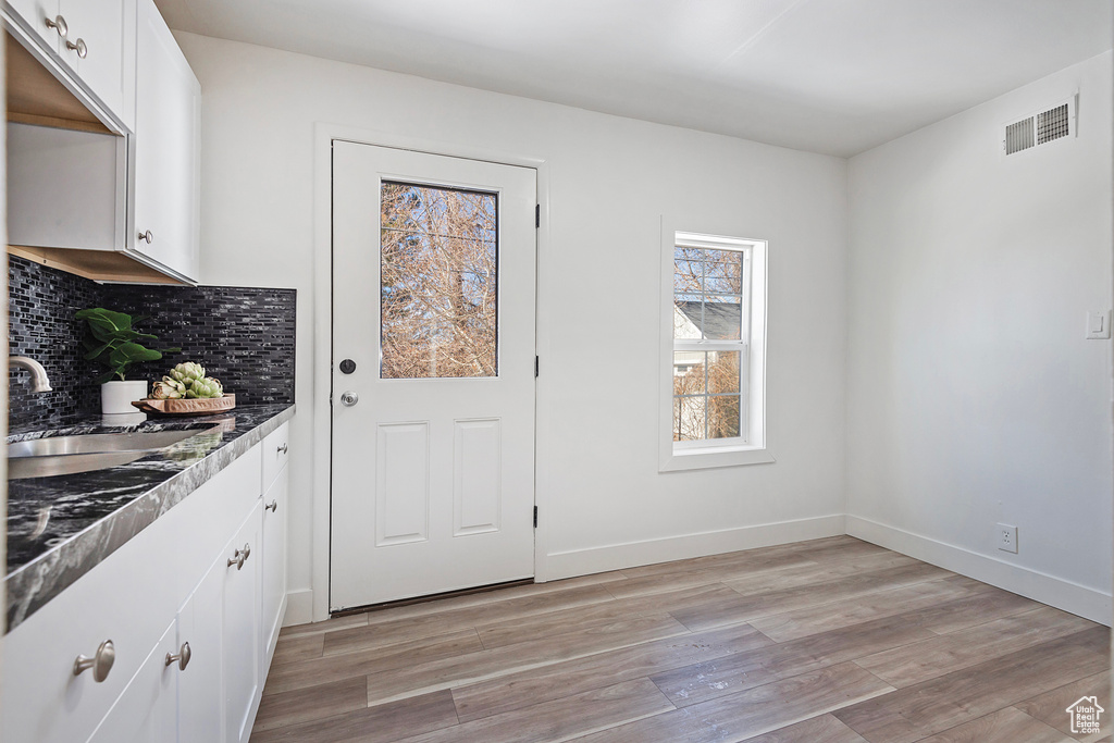 Kitchen featuring tasteful backsplash, white cabinetry, sink, and light hardwood / wood-style flooring