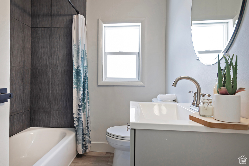 Full bathroom with hardwood / wood-style flooring, vanity, shower / bath combo with shower curtain, and toilet