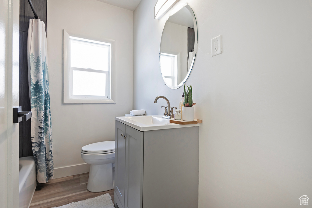 Full bathroom with vanity, hardwood / wood-style flooring, shower / bath combination with curtain, and toilet