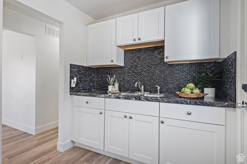 Kitchen with tasteful backsplash, white cabinetry, sink, dark stone countertops, and light hardwood / wood-style flooring