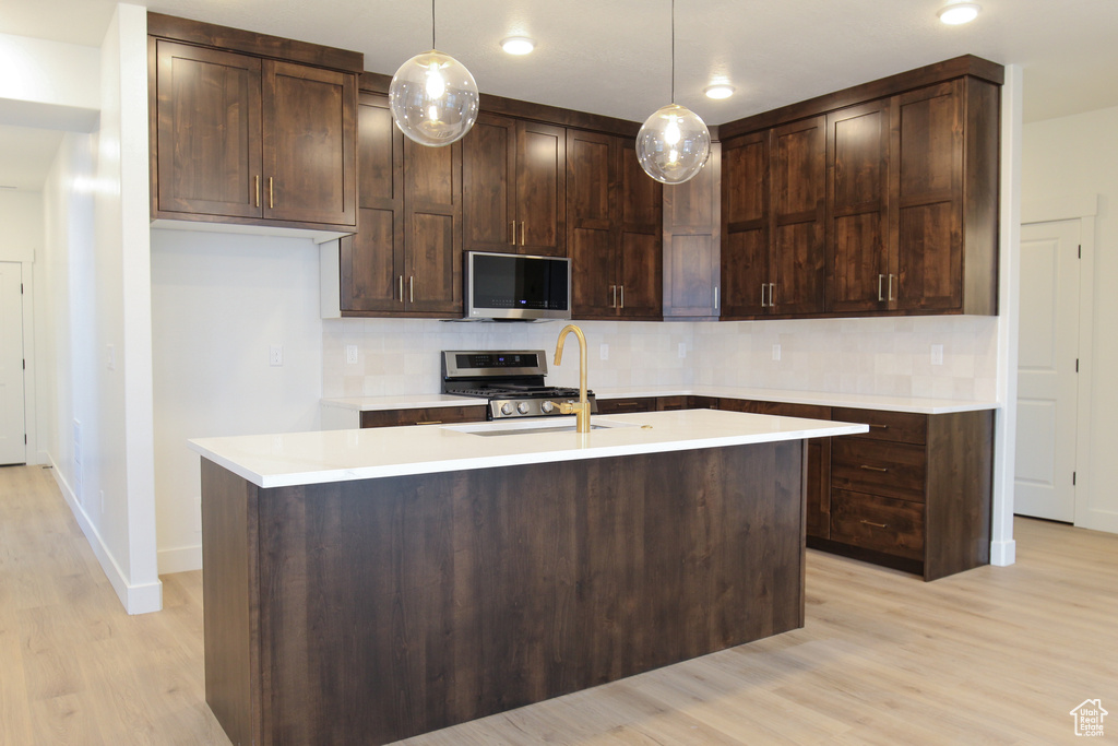 Kitchen featuring stainless steel microwave, range, a sink, light wood-style floors, and backsplash