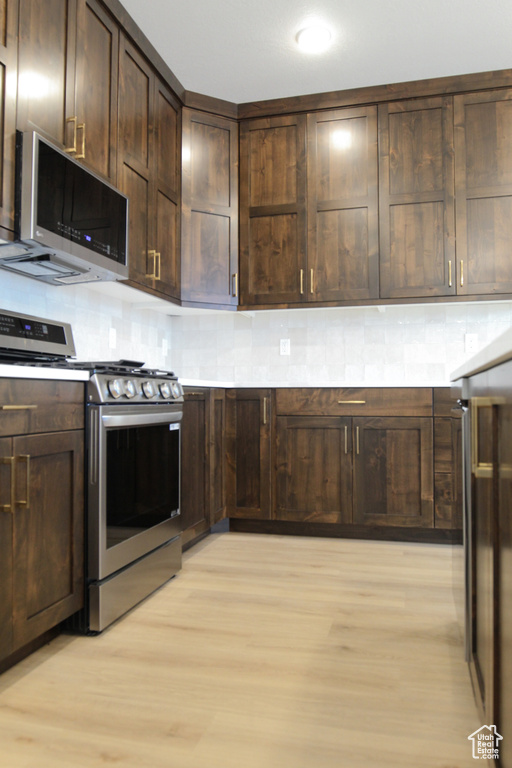 Kitchen featuring appliances with stainless steel finishes, light wood-style flooring, decorative backsplash, and dark brown cabinetry
