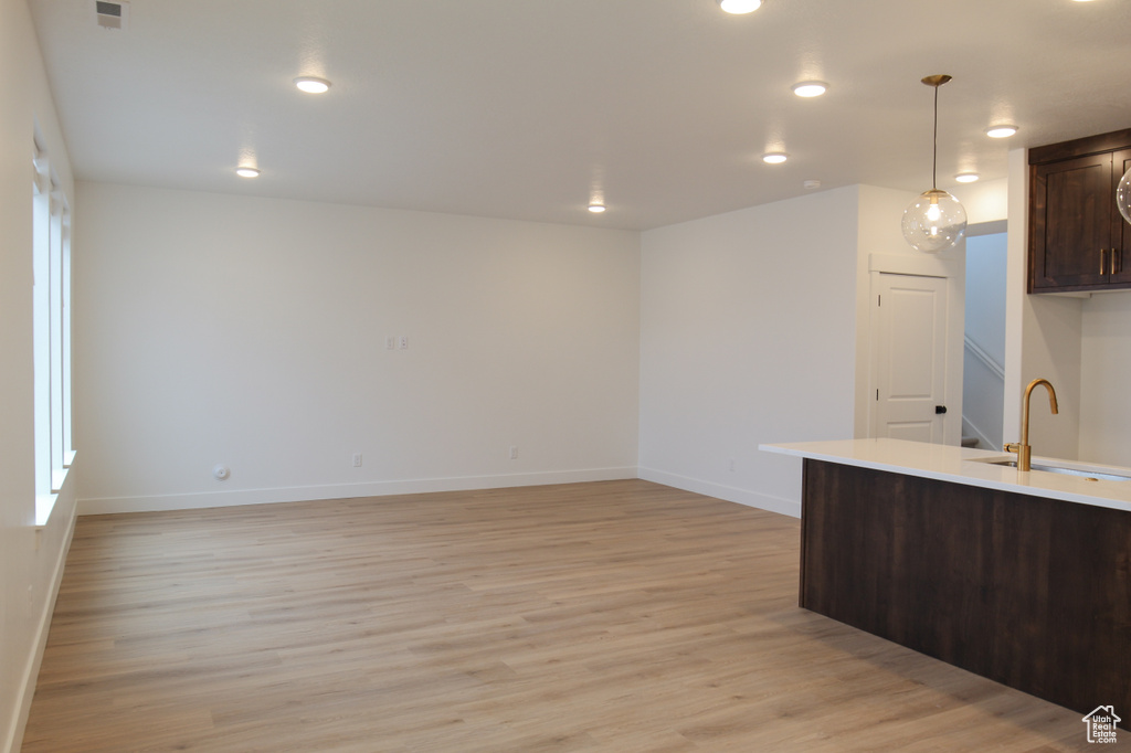 Kitchen with a sink, dark brown cabinets, light wood finished floors, baseboards, and light countertops