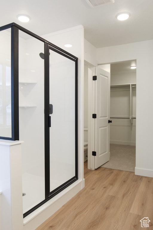 Bathroom with a shower stall, wood finished floors, toilet, and a spacious closet