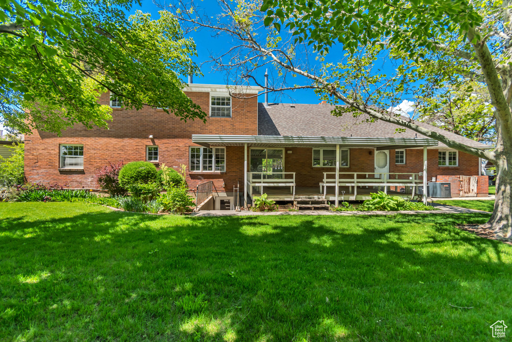 Back of house with a wooden deck, brick siding, a lawn, and central air condition unit