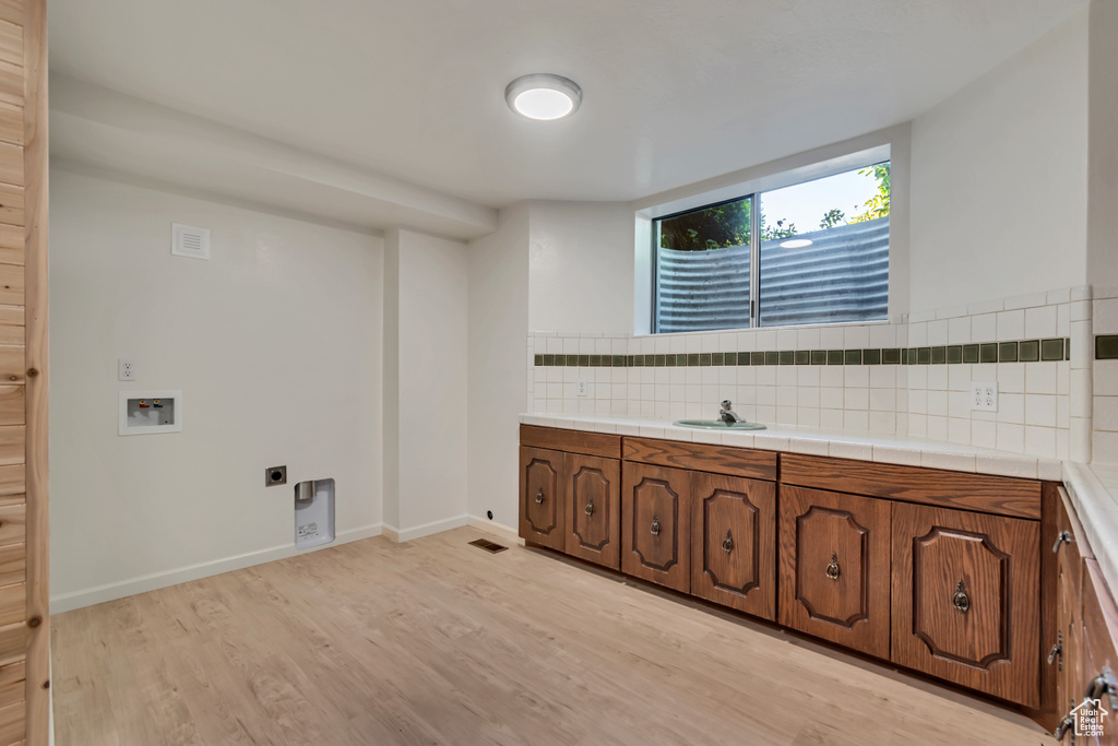 Laundry area with hookup for an electric dryer, light wood finished floors, washer hookup, and cabinet space
