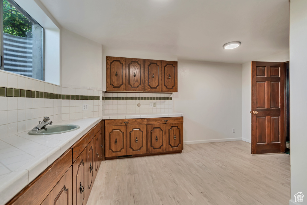 Kitchen featuring tile countertops, a sink, light wood finished floors, and tasteful backsplash
