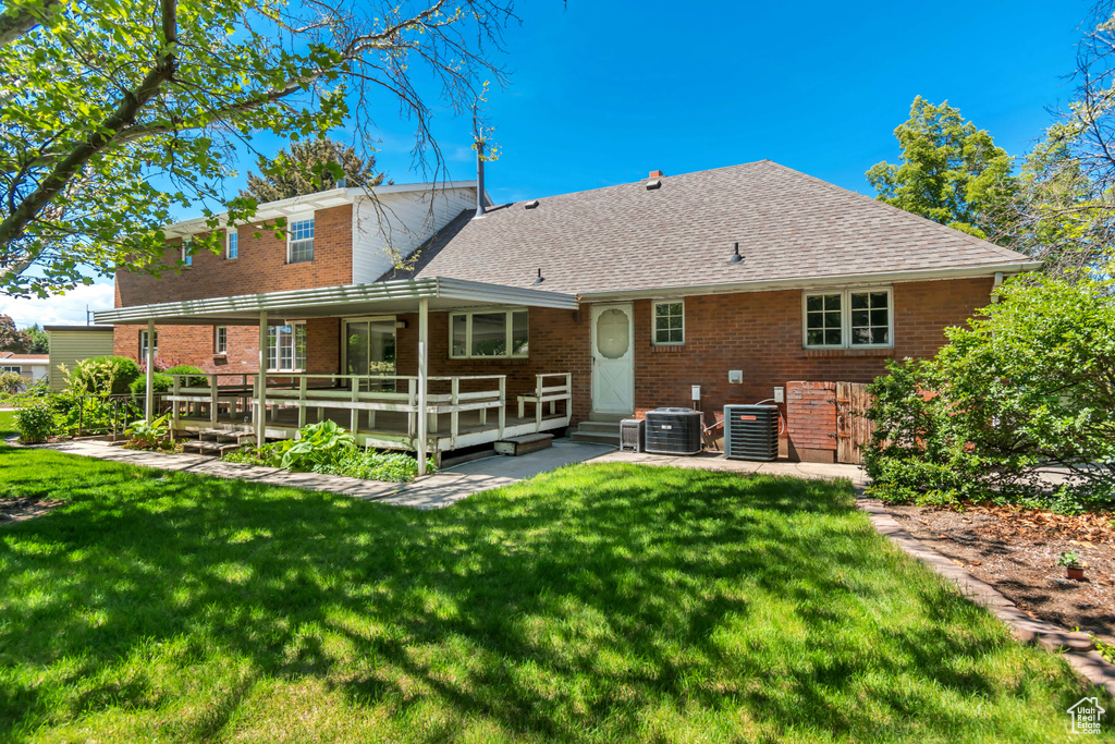 Rear view of property featuring brick siding, a lawn, and a shingled roof