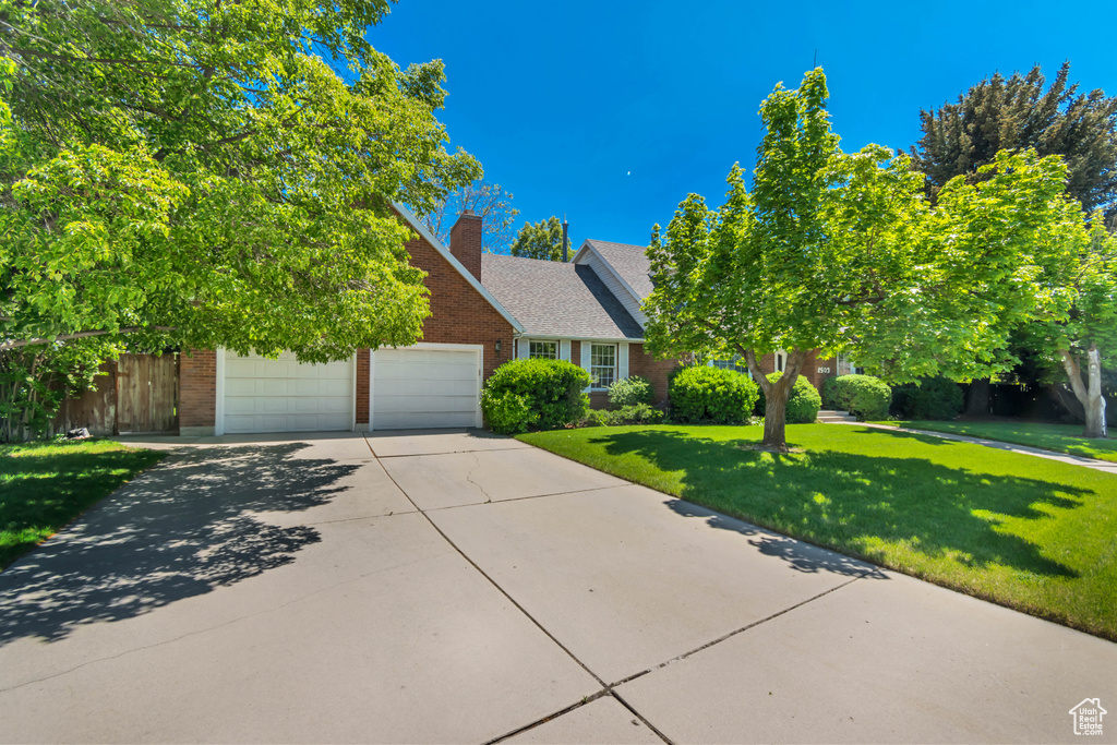 Obstructed view of property with brick siding, concrete driveway, a garage, and a chimney