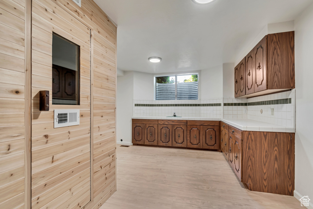 Kitchen featuring backsplash, light wood-type flooring, tile counters, and baseboards