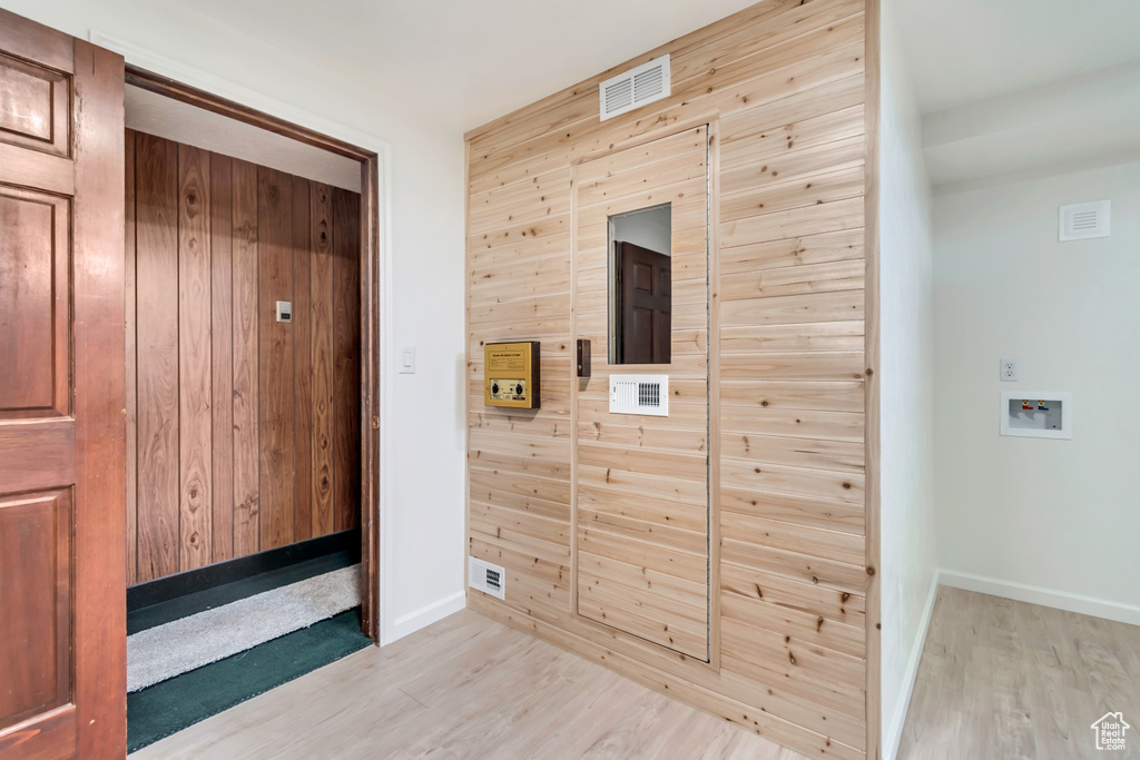 Hall with light wood-style floors, baseboards, and wood walls