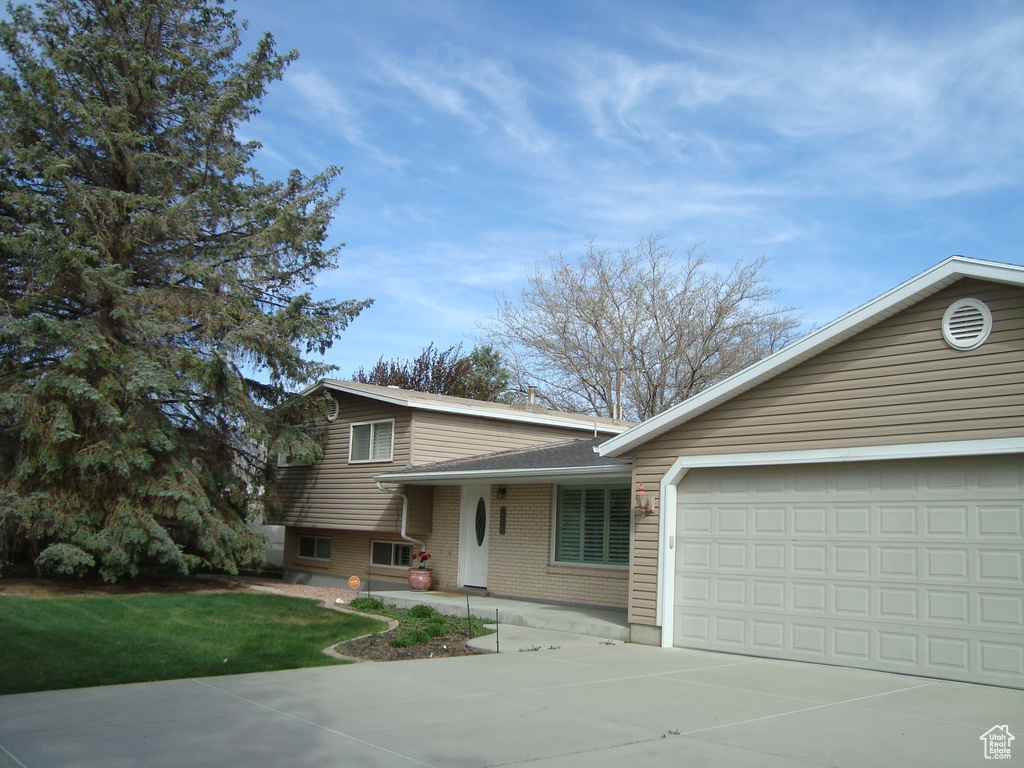 Tri-level home with brick siding, an attached garage, roof with shingles, and concrete driveway