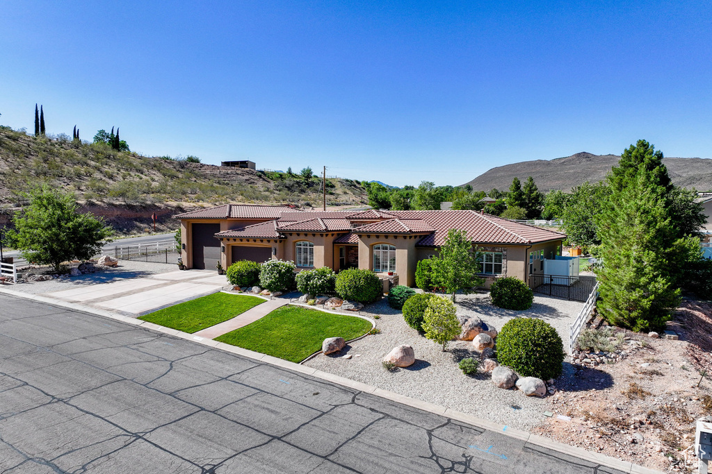 Mediterranean / spanish-style home with an attached garage, concrete driveway, a tile roof, a mountain view, and stucco siding