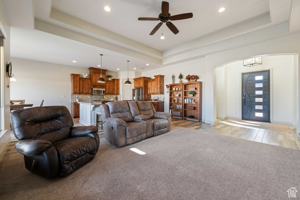 Living area with arched walkways, a raised ceiling, recessed lighting, a ceiling fan, and light wood-style flooring