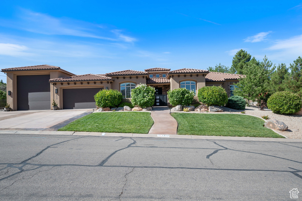 Mediterranean / spanish-style home with stucco siding, a garage, a front lawn, driveway, and a tile roof