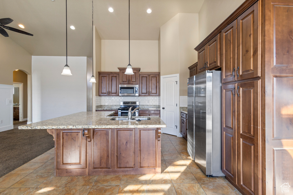 Kitchen featuring a breakfast bar area, hanging light fixtures, appliances with stainless steel finishes, a towering ceiling, and decorative backsplash