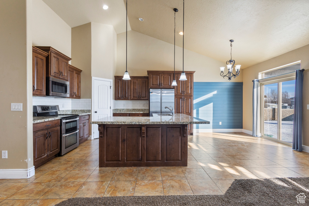Kitchen with pendant lighting, sink, stainless steel appliances, light stone counters, and an island with sink