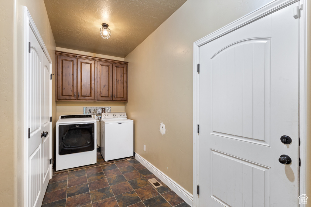 Washroom with washer and clothes dryer, cabinets, and a textured ceiling
