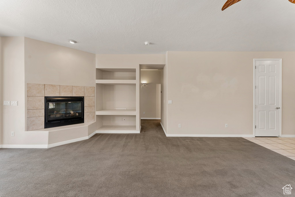 Unfurnished living room featuring a textured ceiling, carpet flooring, built in features, baseboards, and tile patterned flooring