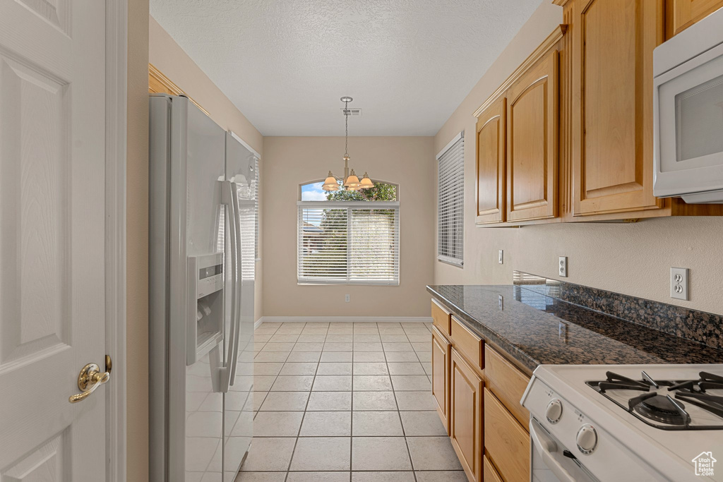 Kitchen with white appliances, a chandelier, baseboards, light tile patterned floors, and hanging light fixtures