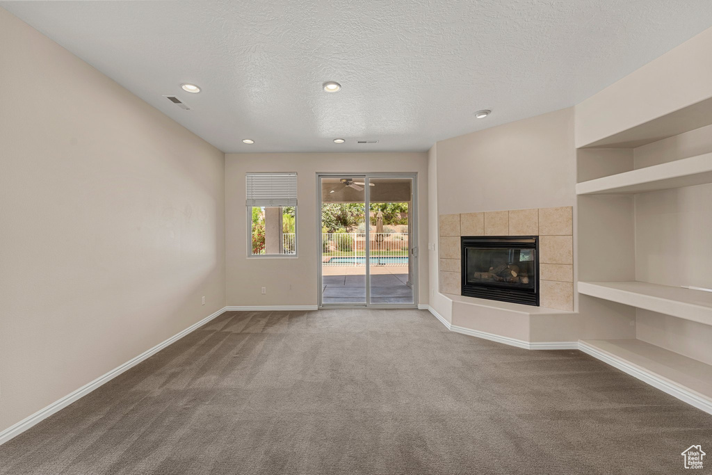 Unfurnished living room with carpet flooring, baseboards, a tile fireplace, a textured ceiling, and recessed lighting
