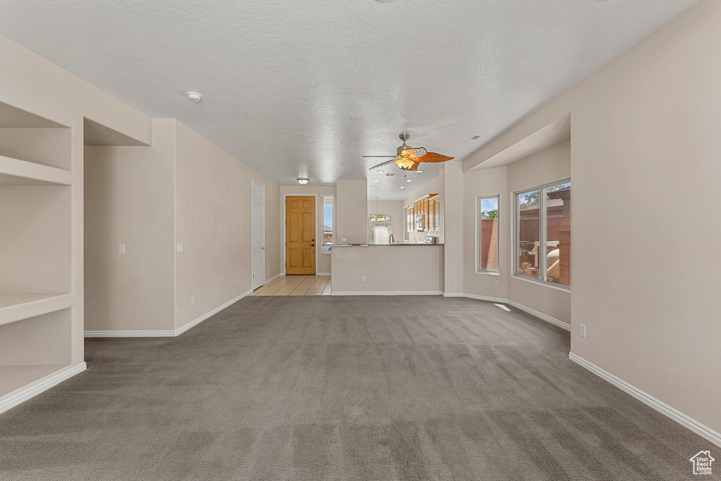 Unfurnished living room featuring carpet flooring, ceiling fan, baseboards, and a textured ceiling