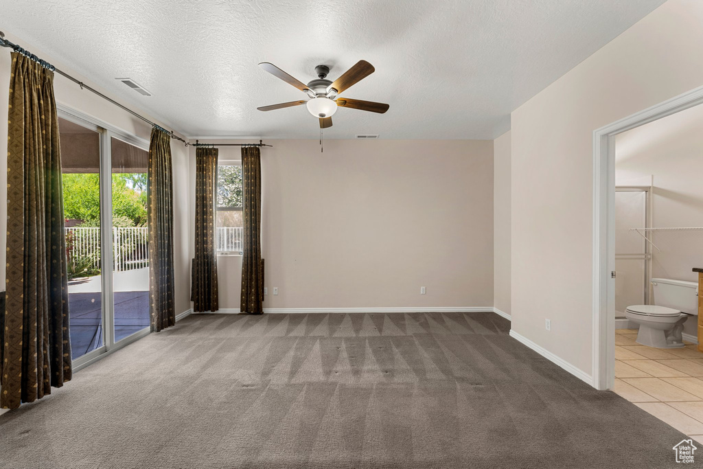 Tiled spare room with a ceiling fan, carpet, baseboards, and a textured ceiling