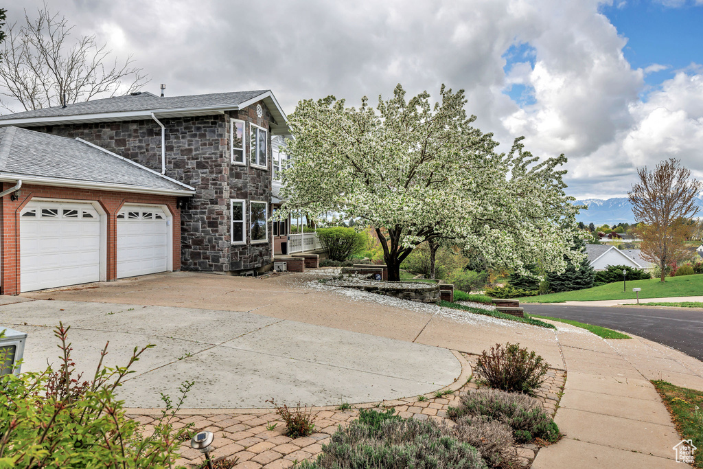 View of side of home featuring concrete driveway, roof with shingles, stone siding, and a garage