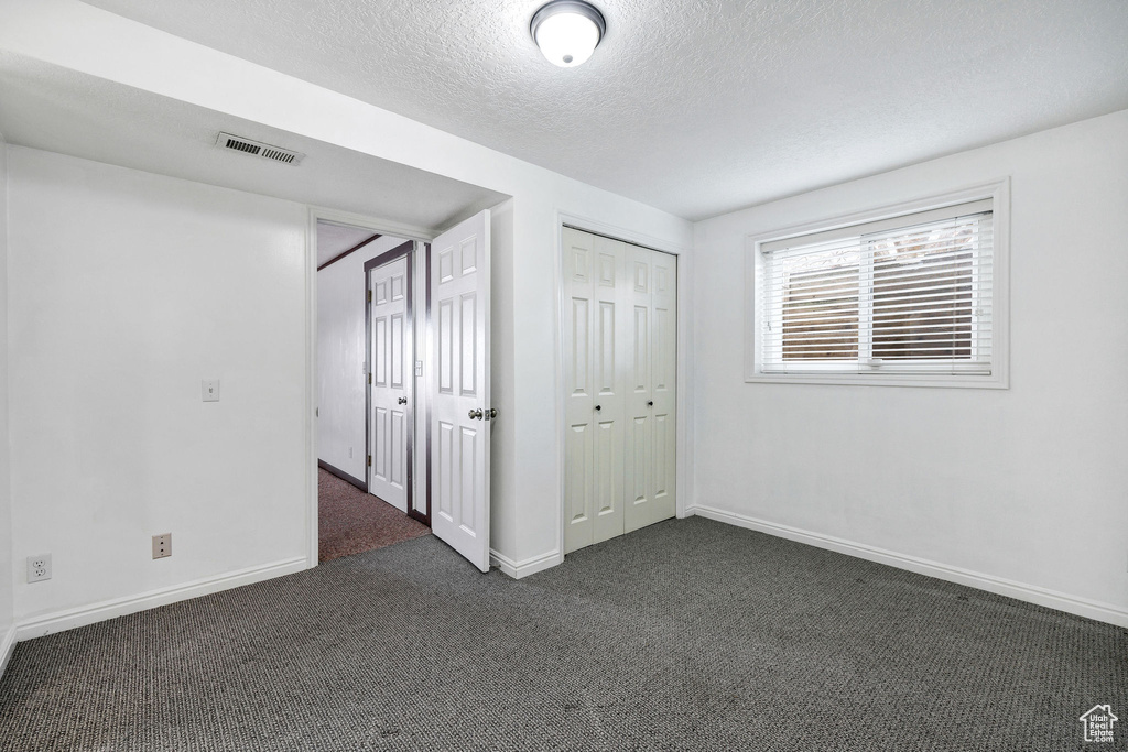 Unfurnished bedroom with a textured ceiling and dark colored carpet