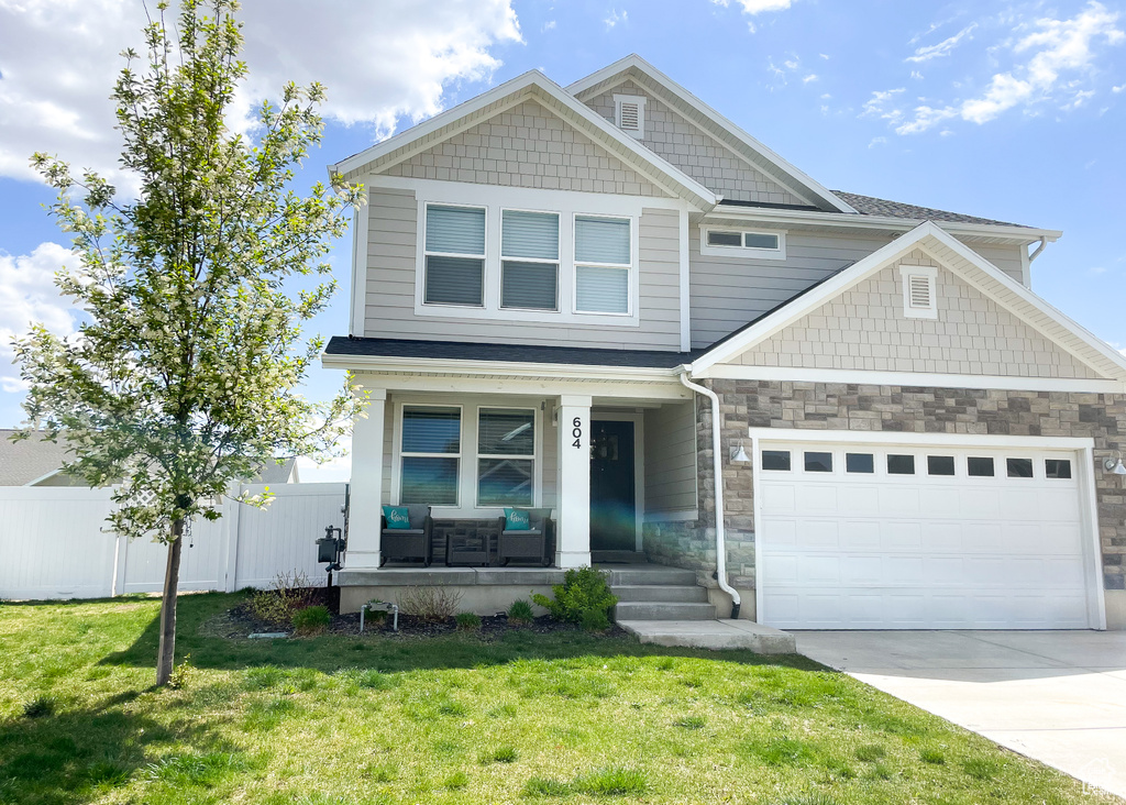 Craftsman-style home with driveway, fence, covered porch, an attached garage, and a front lawn