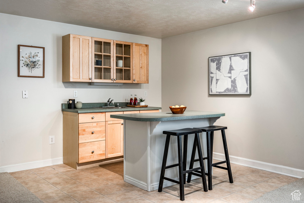 Bar featuring sink, light tile patterned floors, and light brown cabinets