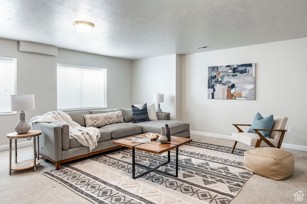 Carpeted living room featuring a wealth of natural light, a wall unit AC, and a textured ceiling