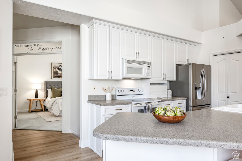 Kitchen with white appliances, white cabinetry, and light wood finished floors