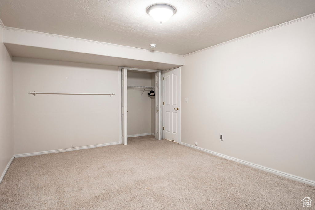 Unfurnished bedroom featuring light colored carpet, ornamental molding, a closet, and a textured ceiling