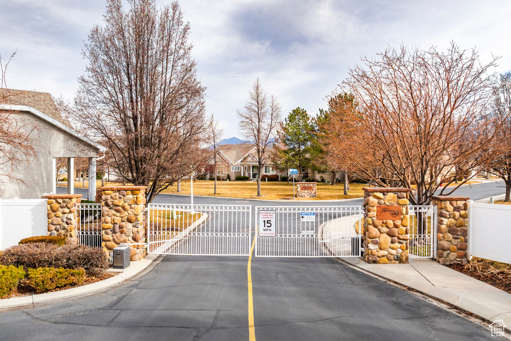 View of asphalt street featuring a gate, curbs, a gated entry, and sidewalks