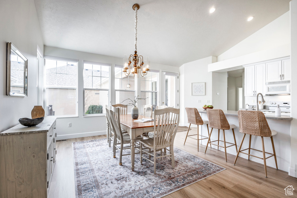 Dining area featuring light hardwood / wood-style flooring, a notable chandelier, and vaulted ceiling