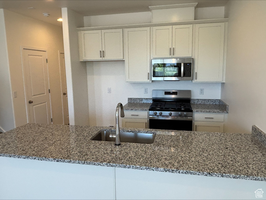 Kitchen with appliances with stainless steel finishes, dark stone countertops, and white cabinets