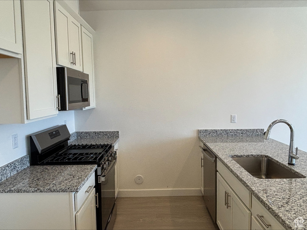 Kitchen with appliances with stainless steel finishes, wood finished floors, light stone countertops, and white cabinets