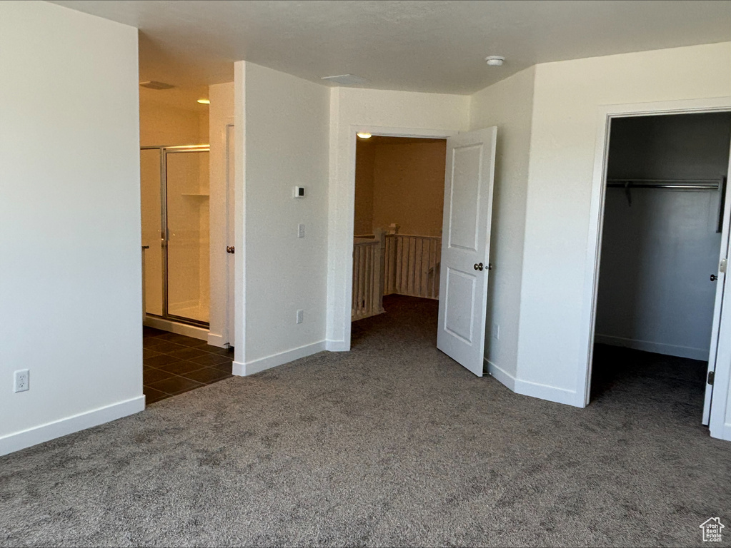 Unfurnished bedroom featuring carpet flooring, a walk in closet, a closet, and ensuite bath