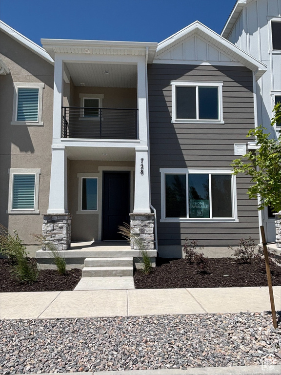 View of front of house with board and batten siding, a balcony, and stone siding