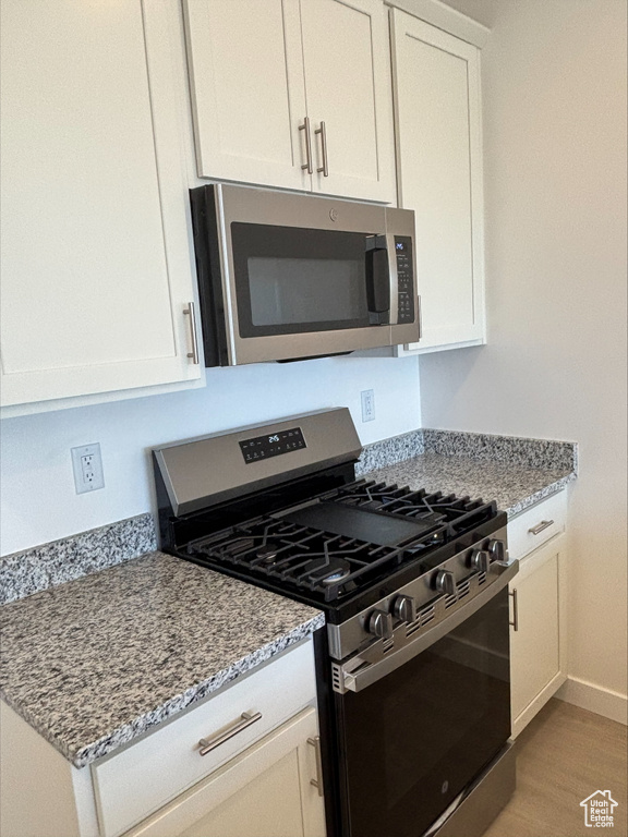 Kitchen with appliances with stainless steel finishes, light wood-type flooring, white cabinets, and light stone counters