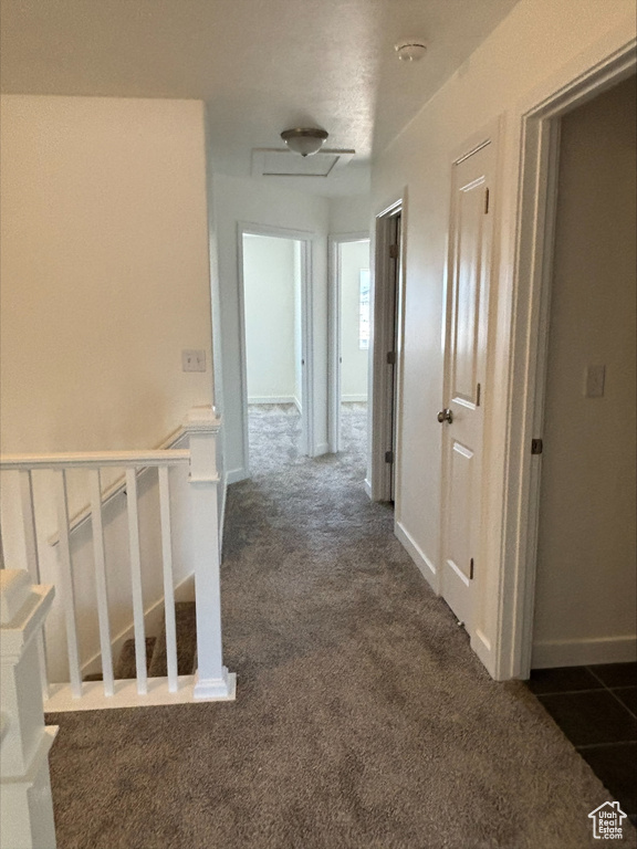 Hall with dark colored carpet and an upstairs landing