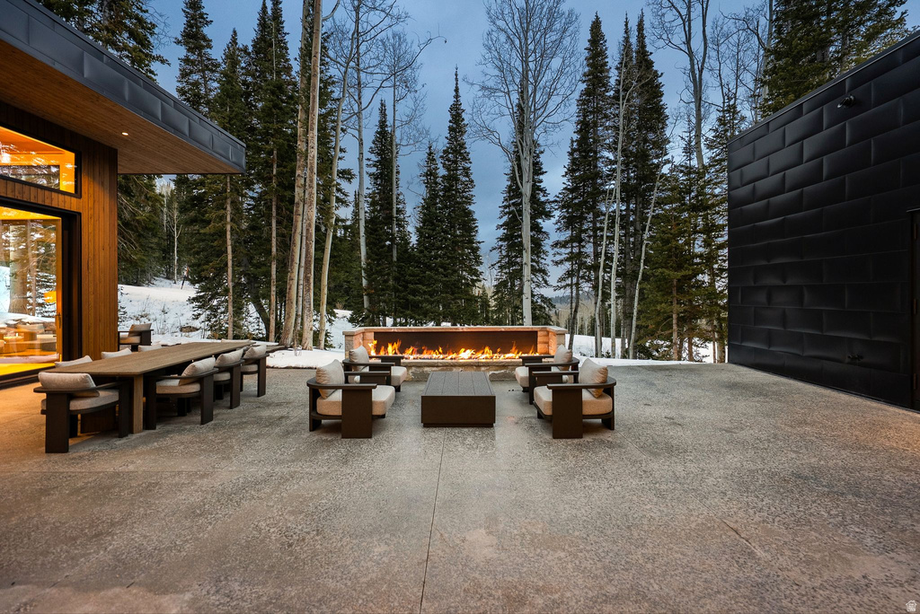 Snow covered patio with a patio, outdoor dining area, an outdoor living space with a fire pit, and view of wooded area