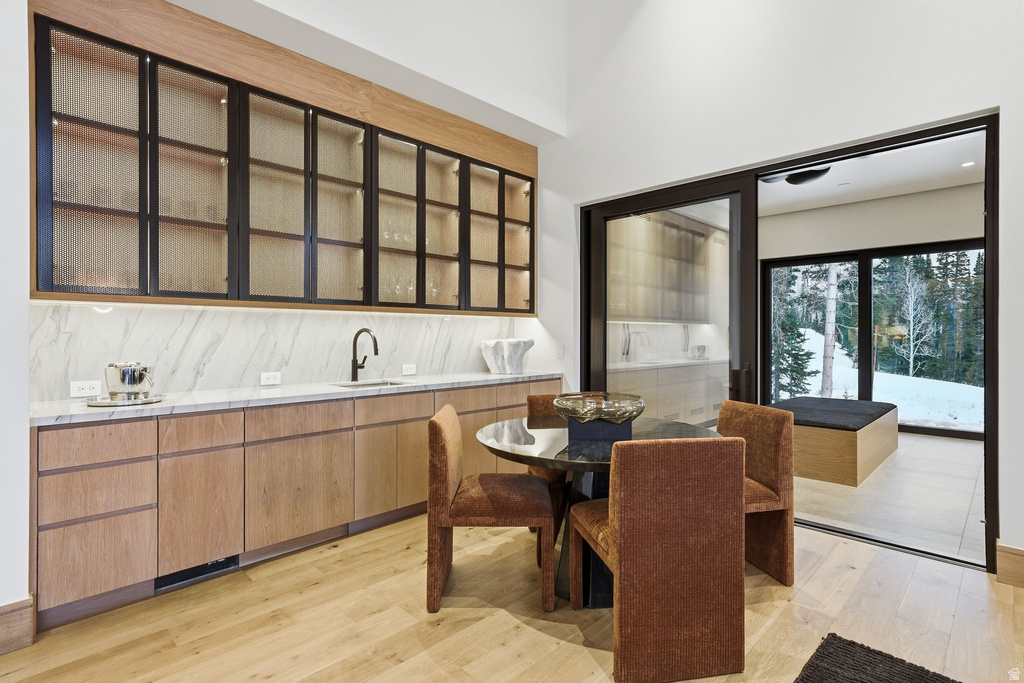 Kitchen featuring light wood-style floors, modern cabinets, glass insert cabinets, light stone countertops, and a high ceiling
