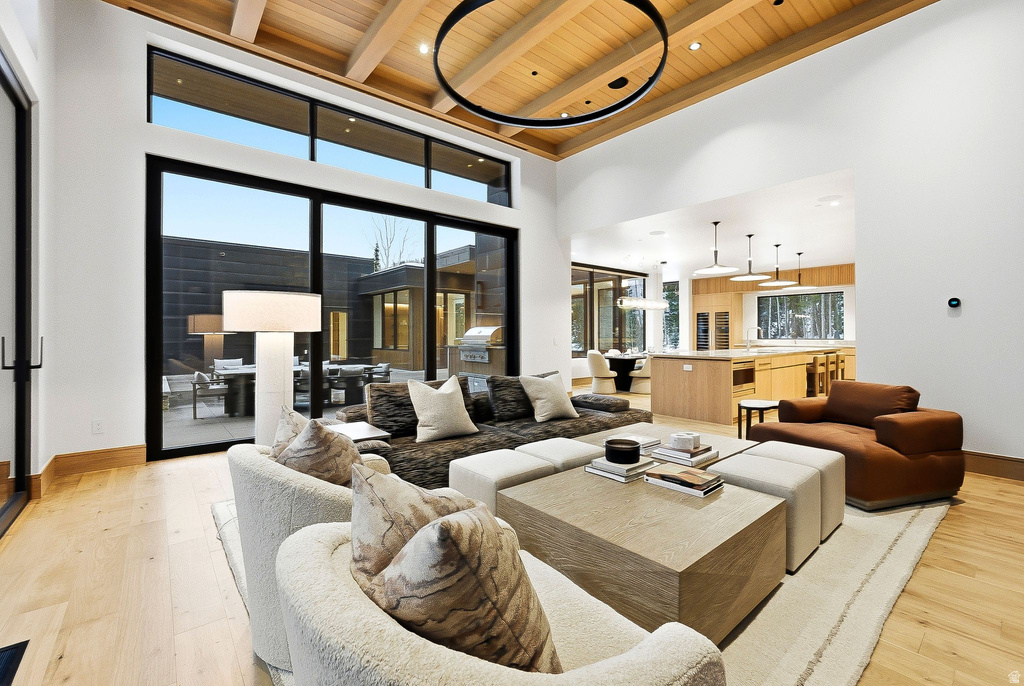 Living area featuring light wood finished floors, a wood ceiling with exposed beams, plenty of natural light, and a high ceiling